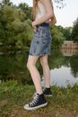 Woman in Blue Denim Skirt and Black and White Sneakers Standing on Green Grass Field during