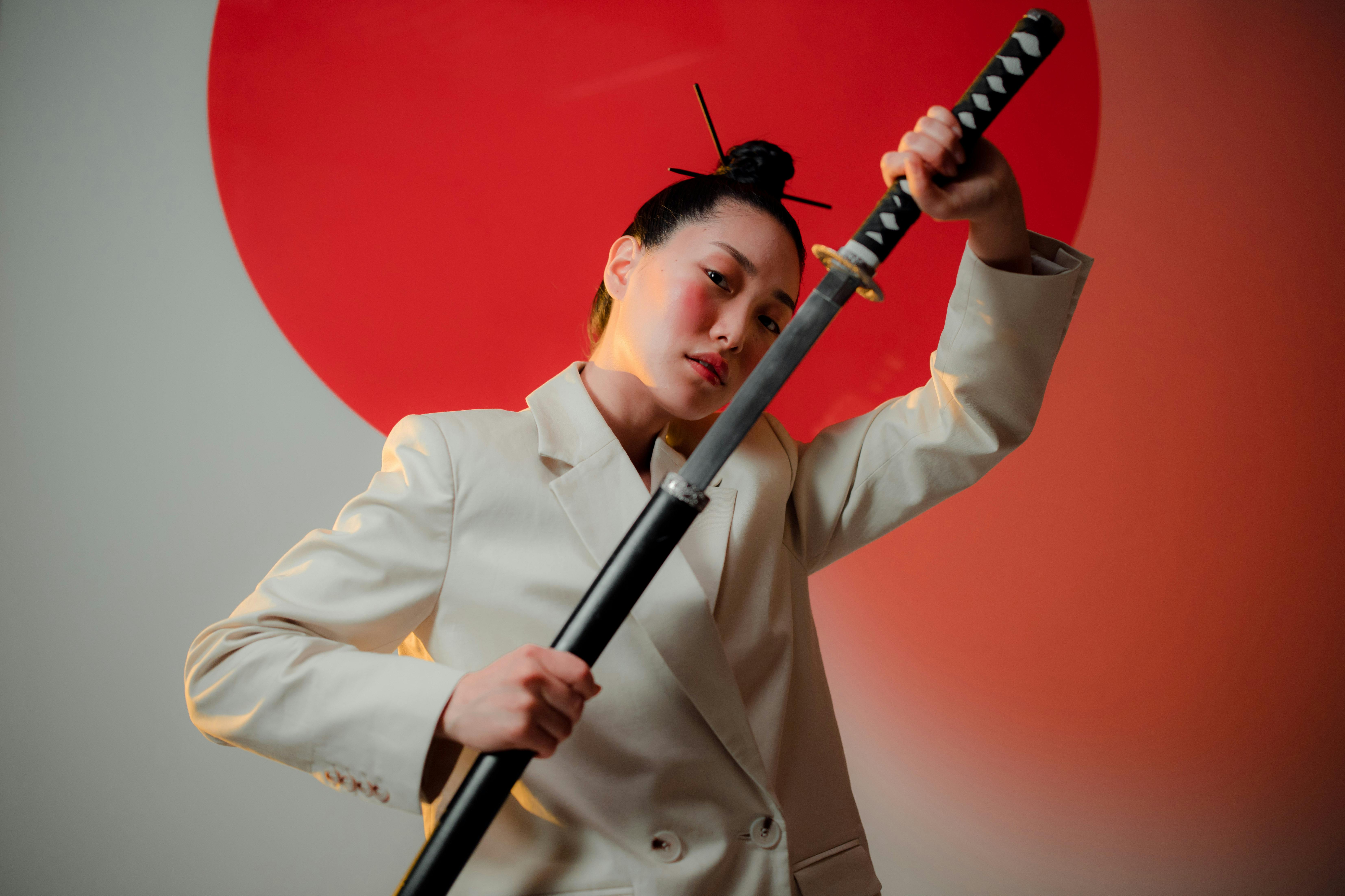 Free Portrait of an Asian woman in a blazer unsheathing a sword with modern artistic styling. Stock Photo