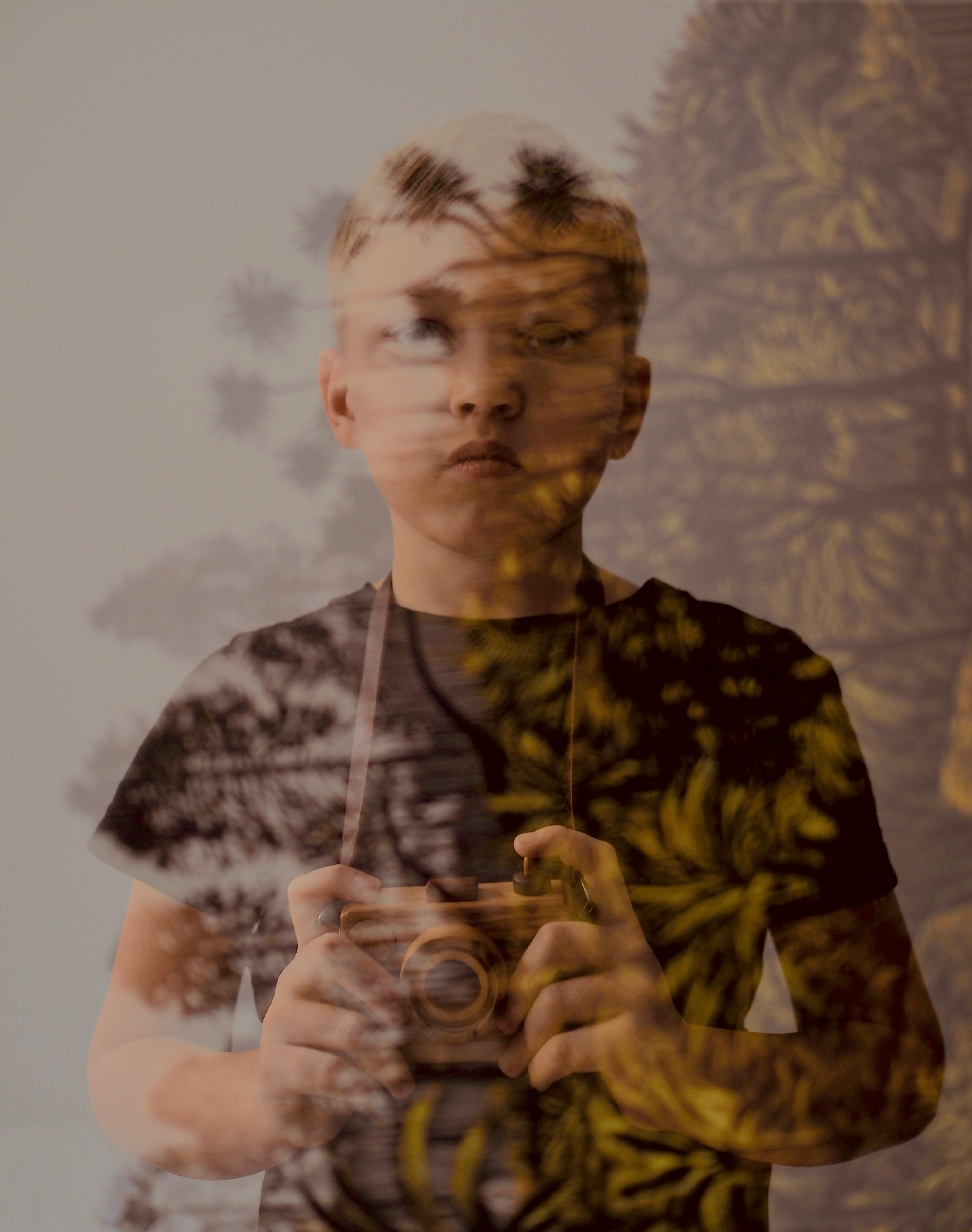 Creative portrait of a boy with a camera reflecting outdoor scenery.