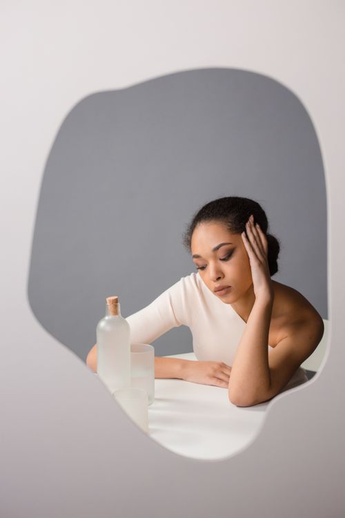 Free A contemplative woman reflected in a mirror with minimalistic background. Stock Photo