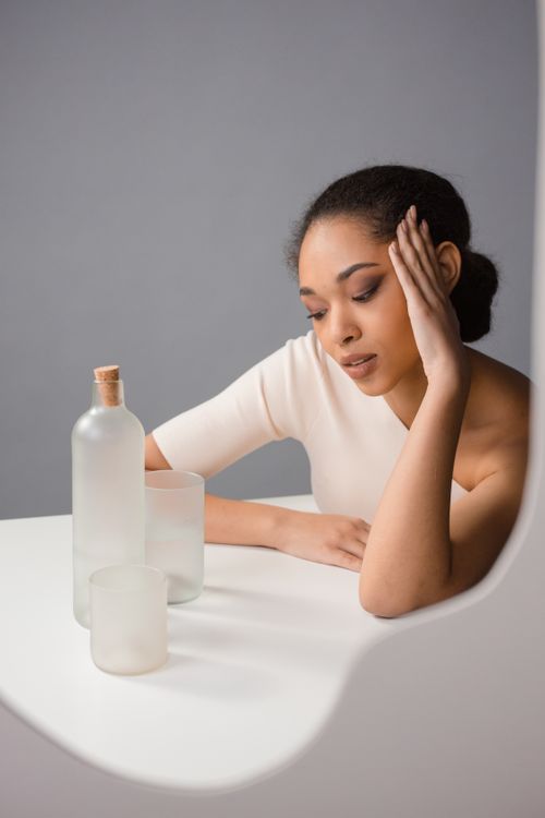 Free Portrait of a fashionable woman in a studio, pondering with frosted glass bottles on table. Stock Photo