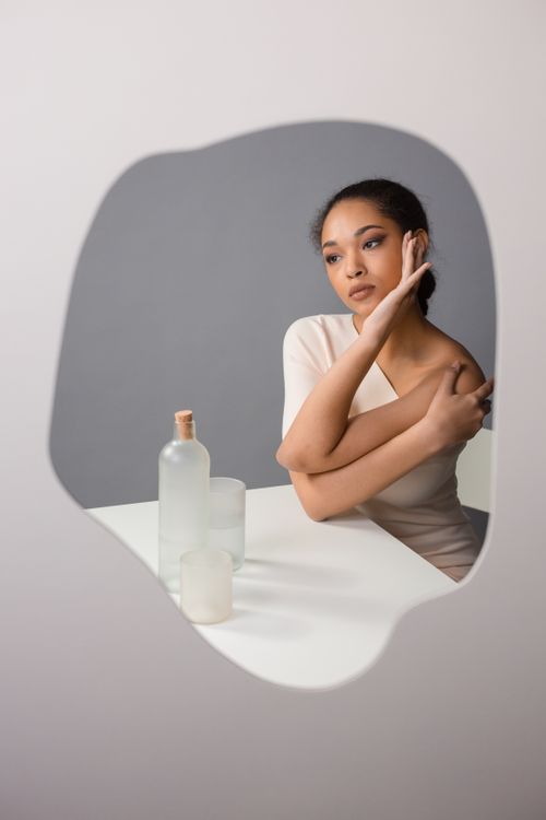 Free Studio portrait of a contemplative woman looking in a mirror with minimalist design and soft lighting. Stock Photo