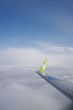 A vibrant green airplane wing contrasting against a clear blue sky and fluffy clouds captured during flight.
