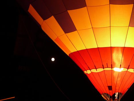 A colorful hot air balloon glowing brightly against the night sky with the moon in the background.