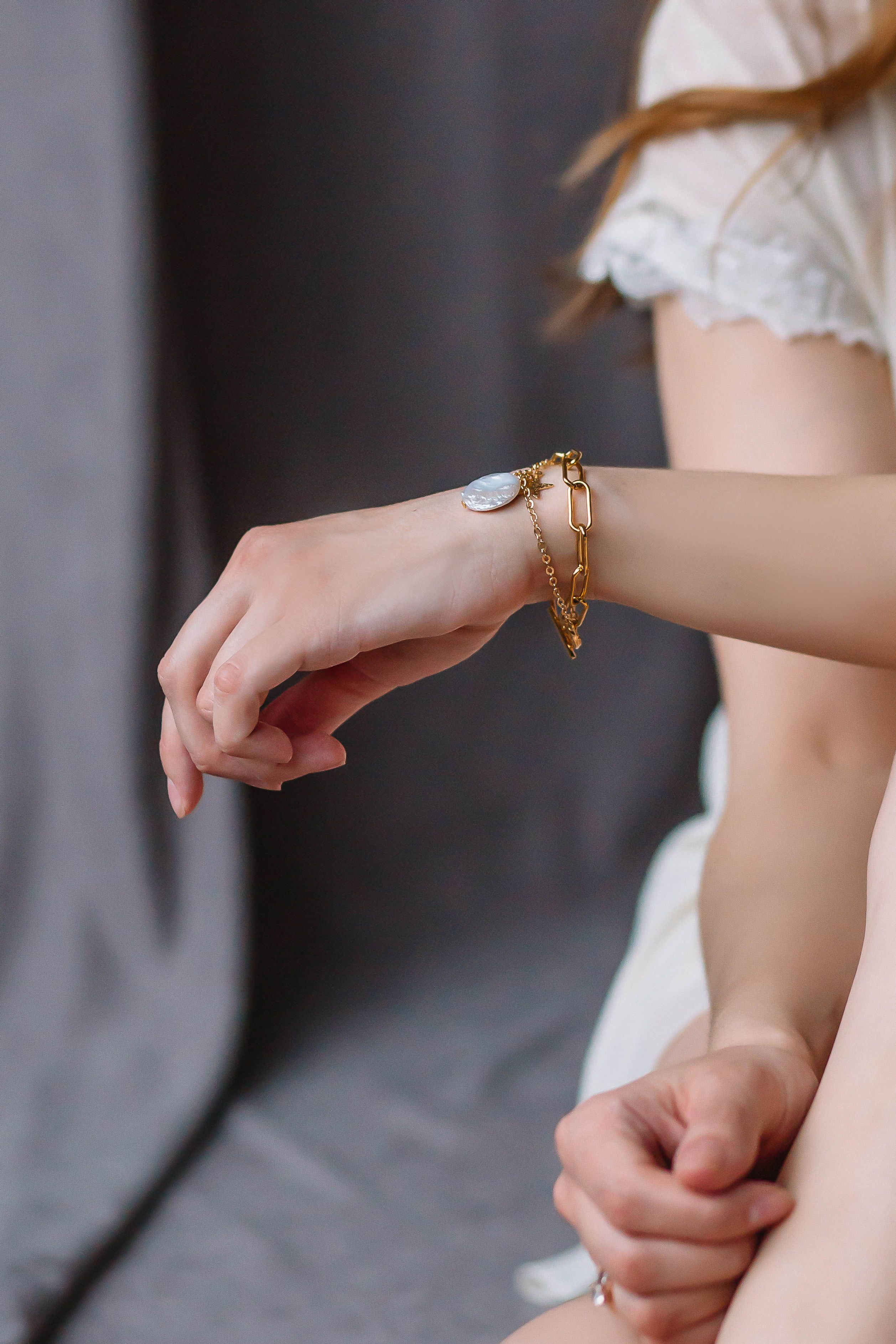 Um close de uma mão feminina usando uma luxuosa pulseira de ouro contra um fundo neutro.