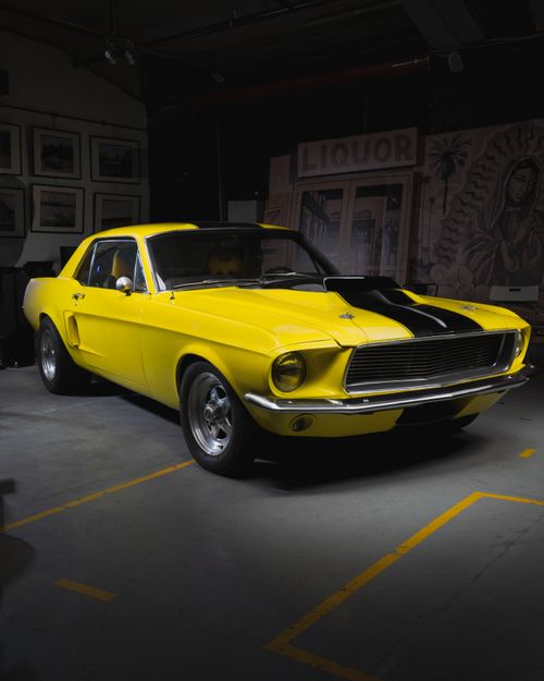 Free Vintage yellow Mustang with black stripes displayed indoors, showcasing classic luxury. Stock Photo