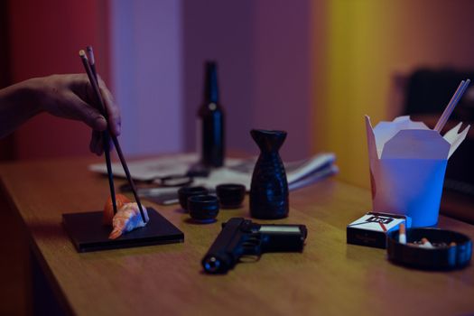 Moody still life featuring sushi, chopsticks, and a pistol on a wooden table.
