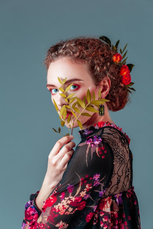 Woman in Black Floral Top With Flowers on Hair Covering Her Face With Leaves