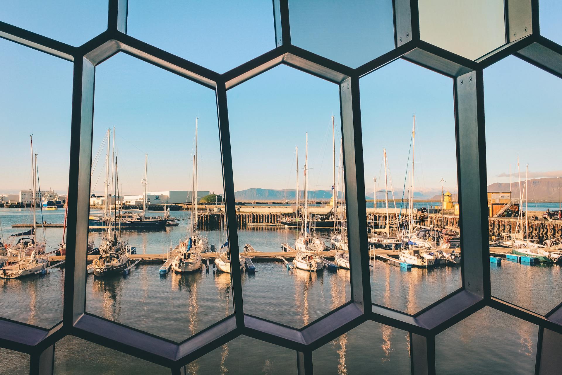 Yachts docked at Reykjavik harbor, seen through architectural glass window panels in Iceland.