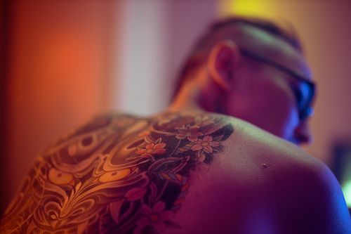 Free Back view of a shirtless man showcasing an artistic tattoo with vivid colors indoors. Stock Photo