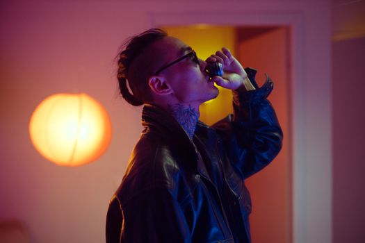 Side view of a stylish man drinking from a cup in a moody, ambient-lit room.