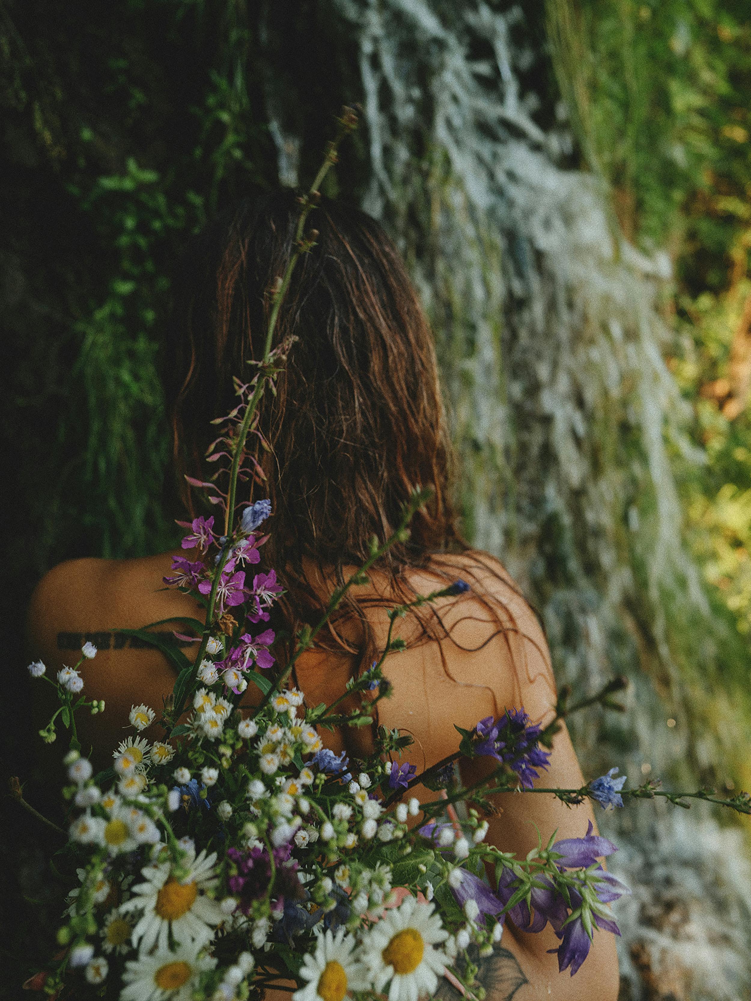 Woman standing by a waterfall holding vibrant wildflowers, creating a serene blend of nature and beauty.