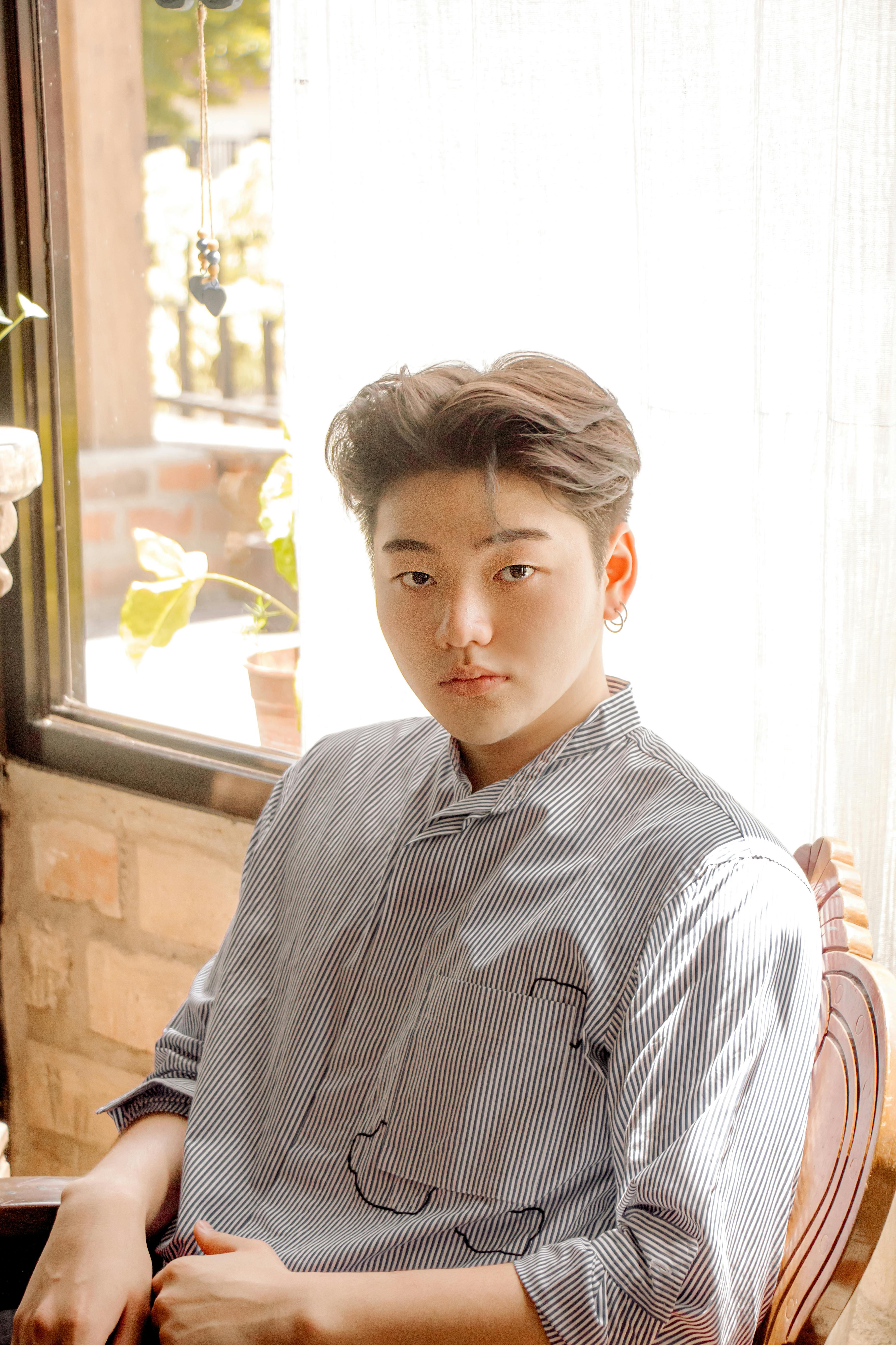 A young man in a striped shirt sits by the window in a cozy indoor setting.
