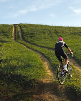 A cyclist rides uphill on a grassy path in Belgorod, Russia, during a sunny day.