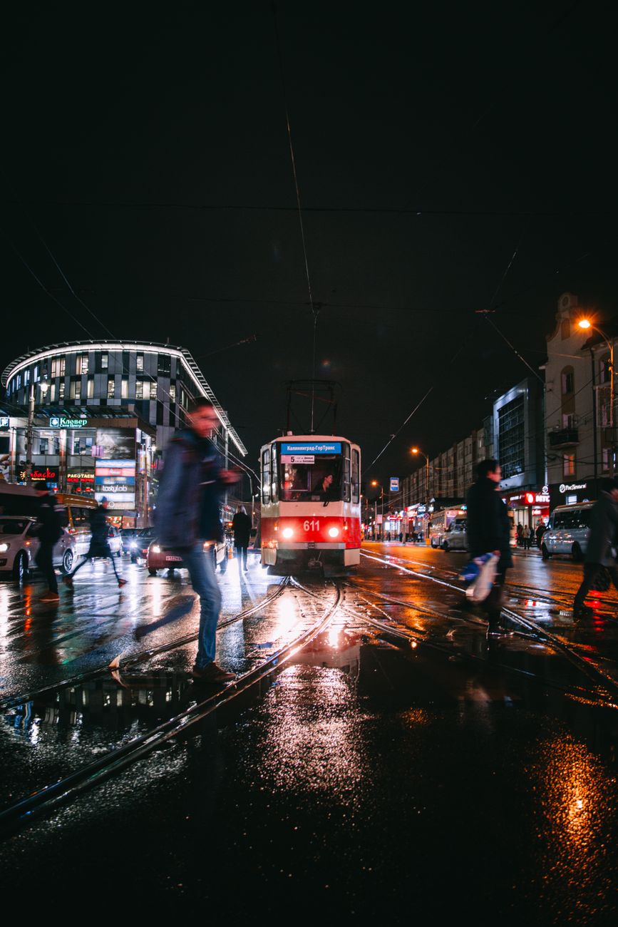 City street at night with a tram, people, and vibrant lights creating an urban atmosphere.
