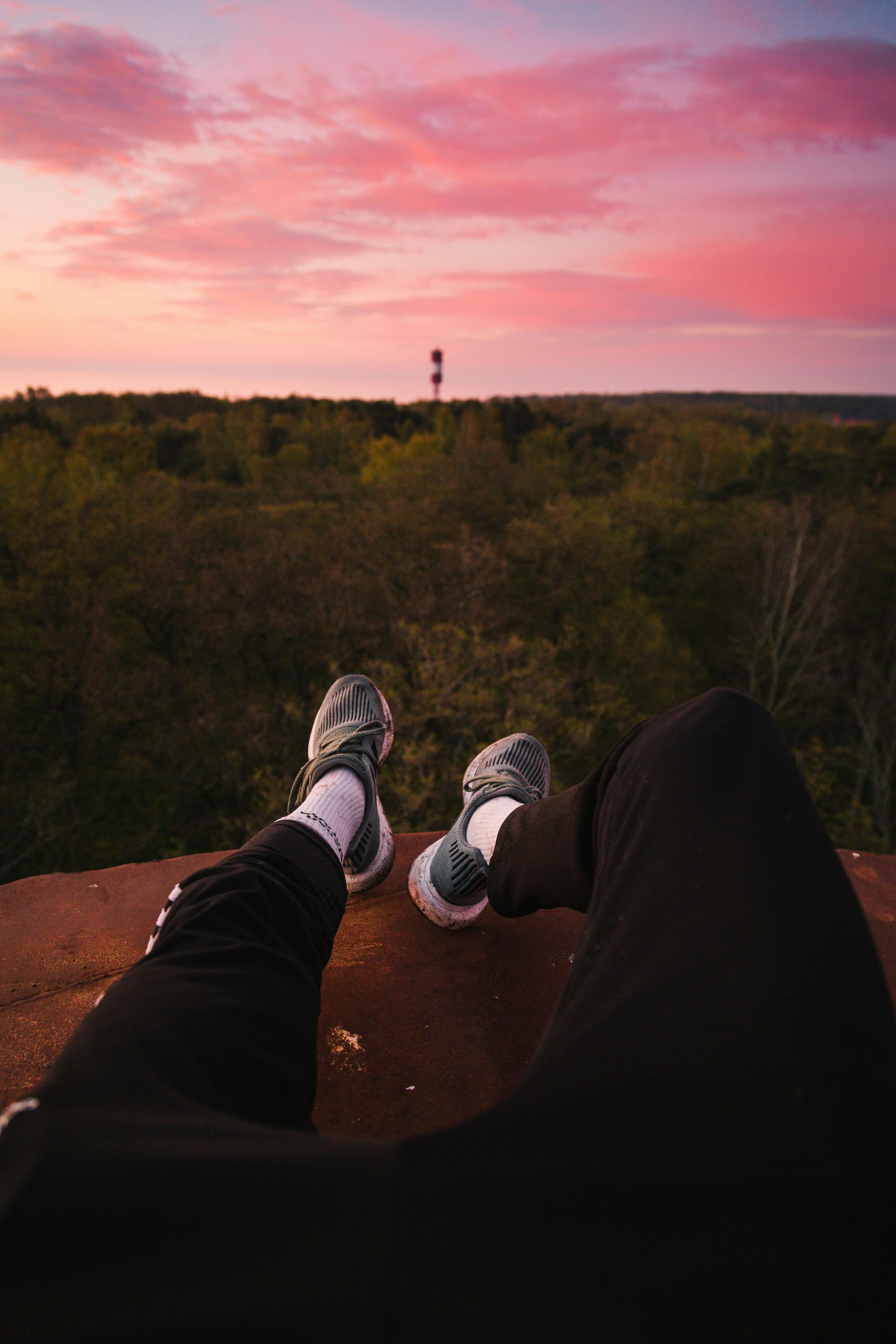 person in black pants and gray sneakers sitting on brown rock during dusk