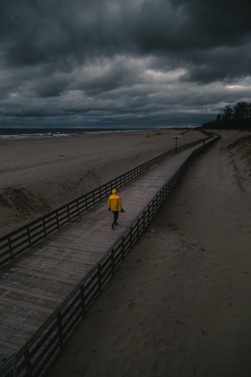 Person Walking On Paved Walkway Under Dark Clouds