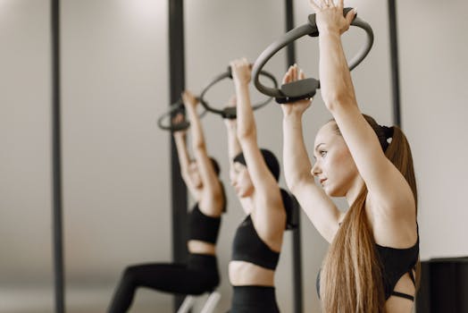 Three women engaged in fitness training using Pilates rings inside a modern gym setting.