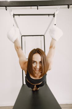 Smiling woman practicing fitness exercises indoors on gym apparatus.