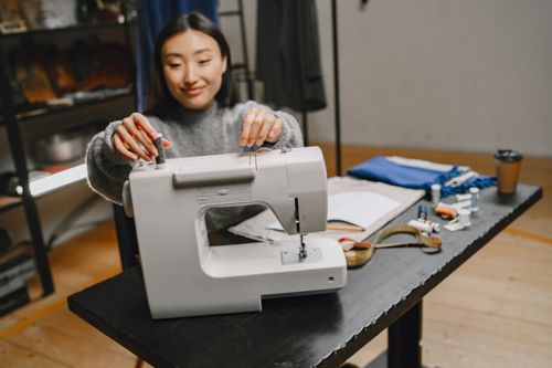 Free Asian woman sewing with a machine in a design workshop. Tools and fabrics on table. Stock Photo