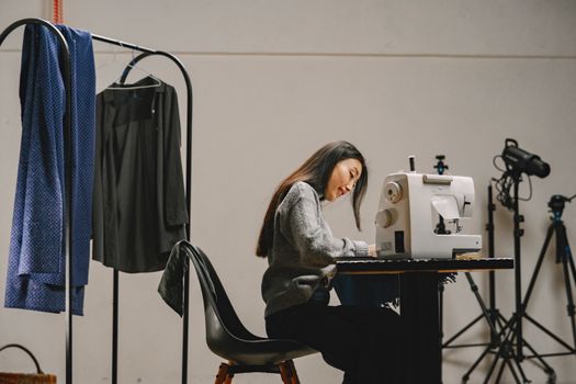 A female fashion designer works diligently at her sewing machine in a studio setting.