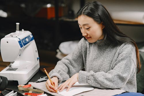 A Woman in Gray Sweater Making Patterns using a Fabric