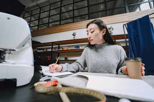 Free Asian woman fashion designer working on sketches with sewing machine and coffee. Stock Photo