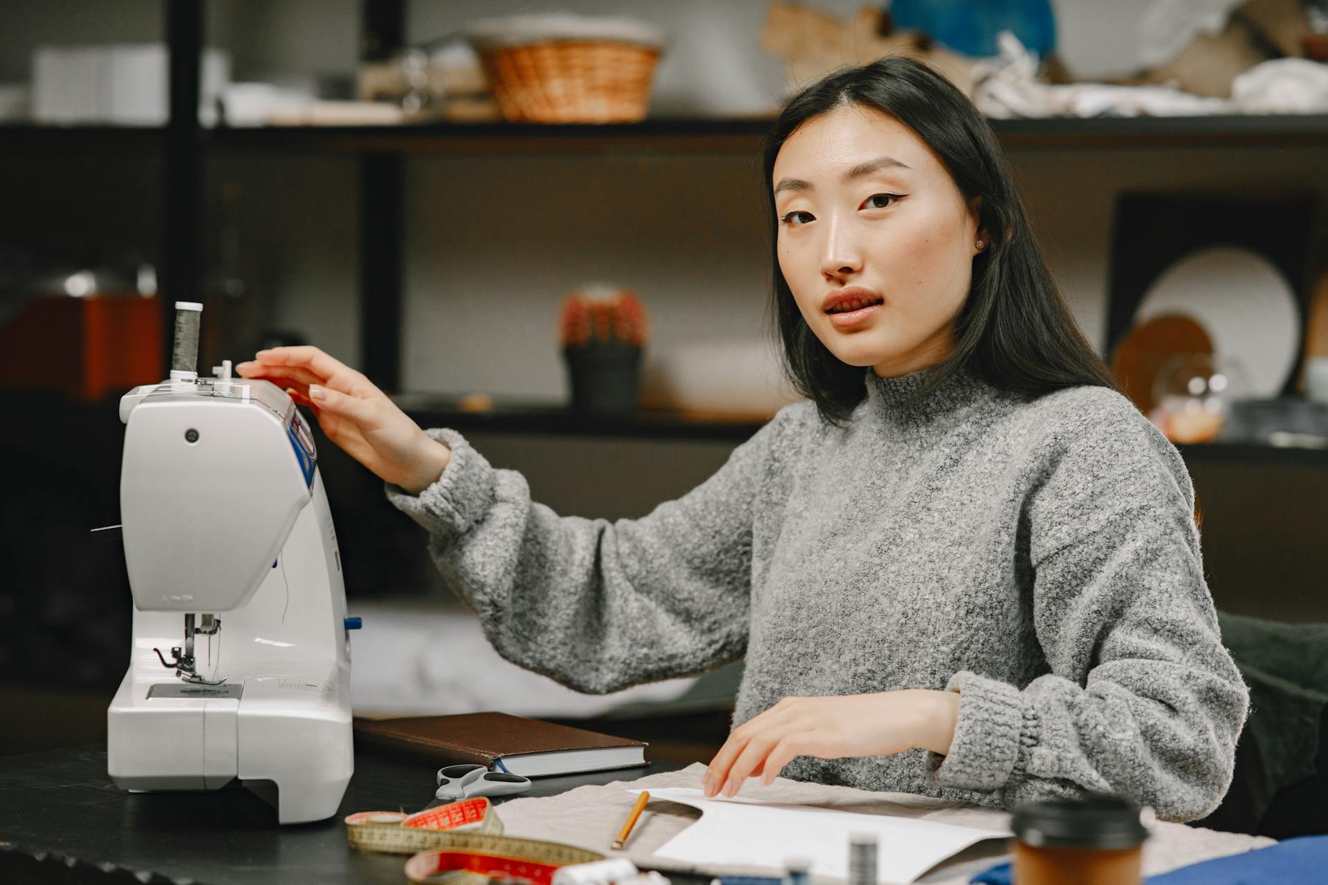 Asian woman dressmaker in a cozy atelier working with a sewing machine, representing small business and creativity.