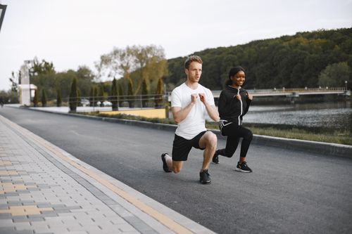 Free A fit couple exercises by a scenic riverside, performing lunges in activewear, showcasing outdoor fitness. Stock Photo