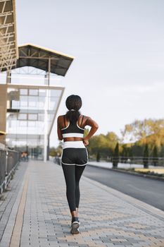 Back view of a woman jogging in activewear along a scenic urban walkway.