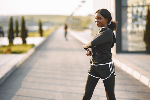 Free Woman in activewear stretches on a sunny morning outdoors, promoting wellness. Stock Photo