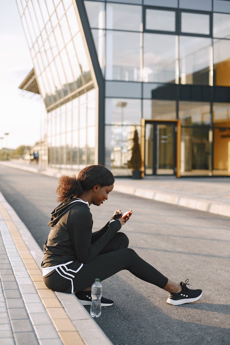 Woman Sitting At A Gutter Using A Cellphone