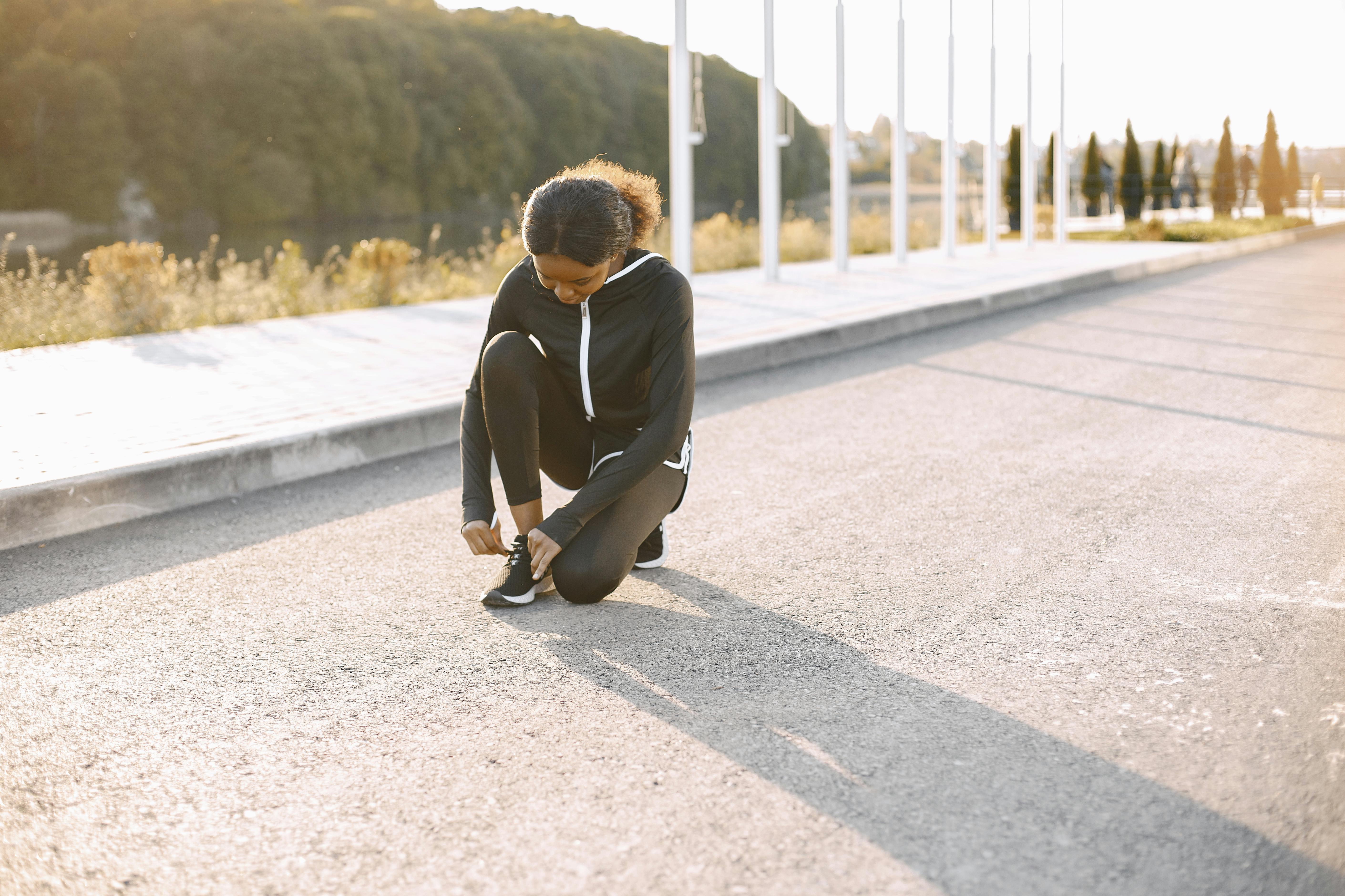 Woman lacing up running shoes, sun rising, park path, determination.