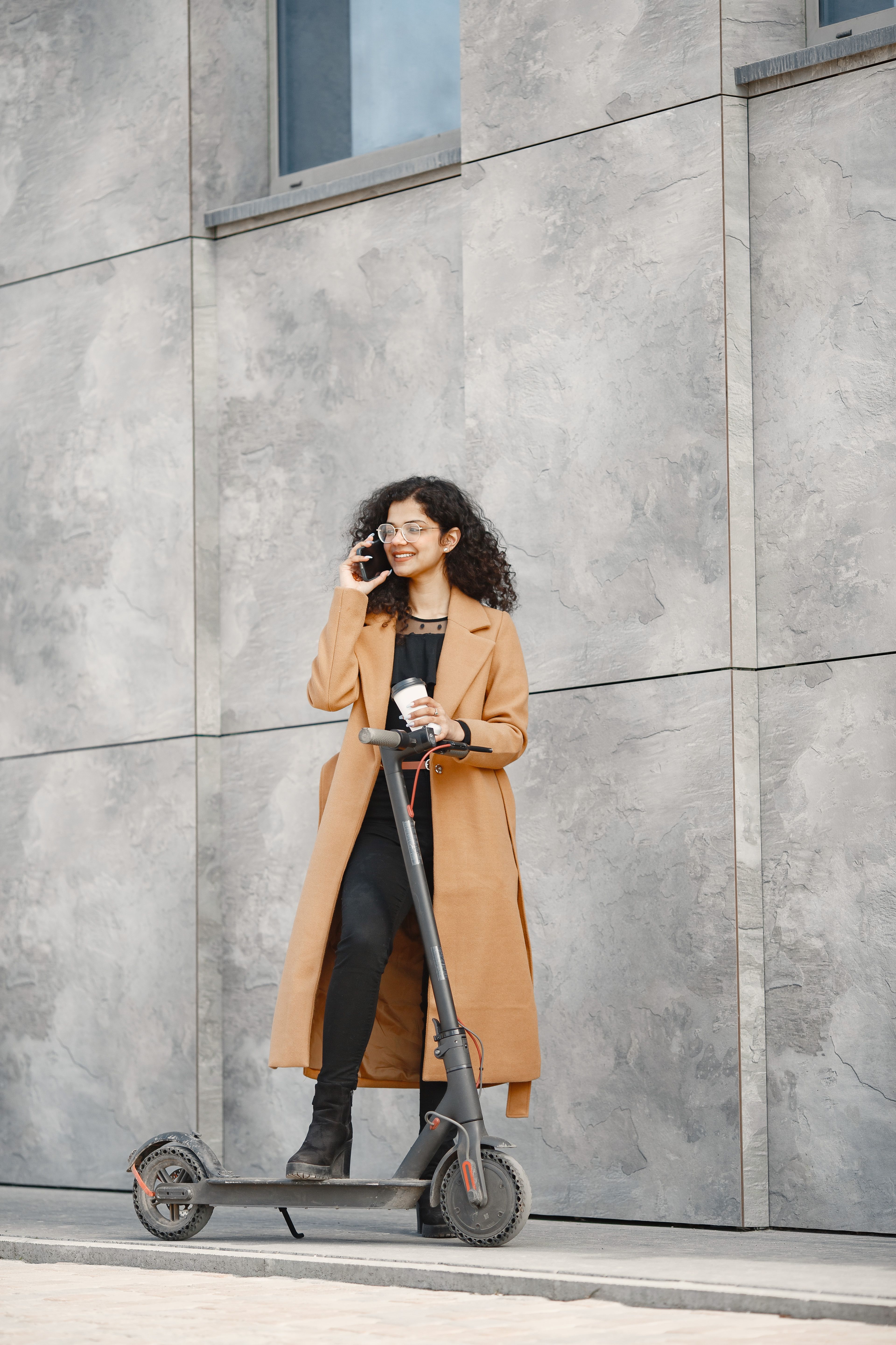 A Woman in Brown Coat Standing Beside Gray Concrete Wall · Free Stock Photo