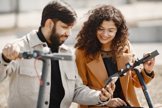 A cheerful couple explores outdoors with electric scooters while using a smartphone.