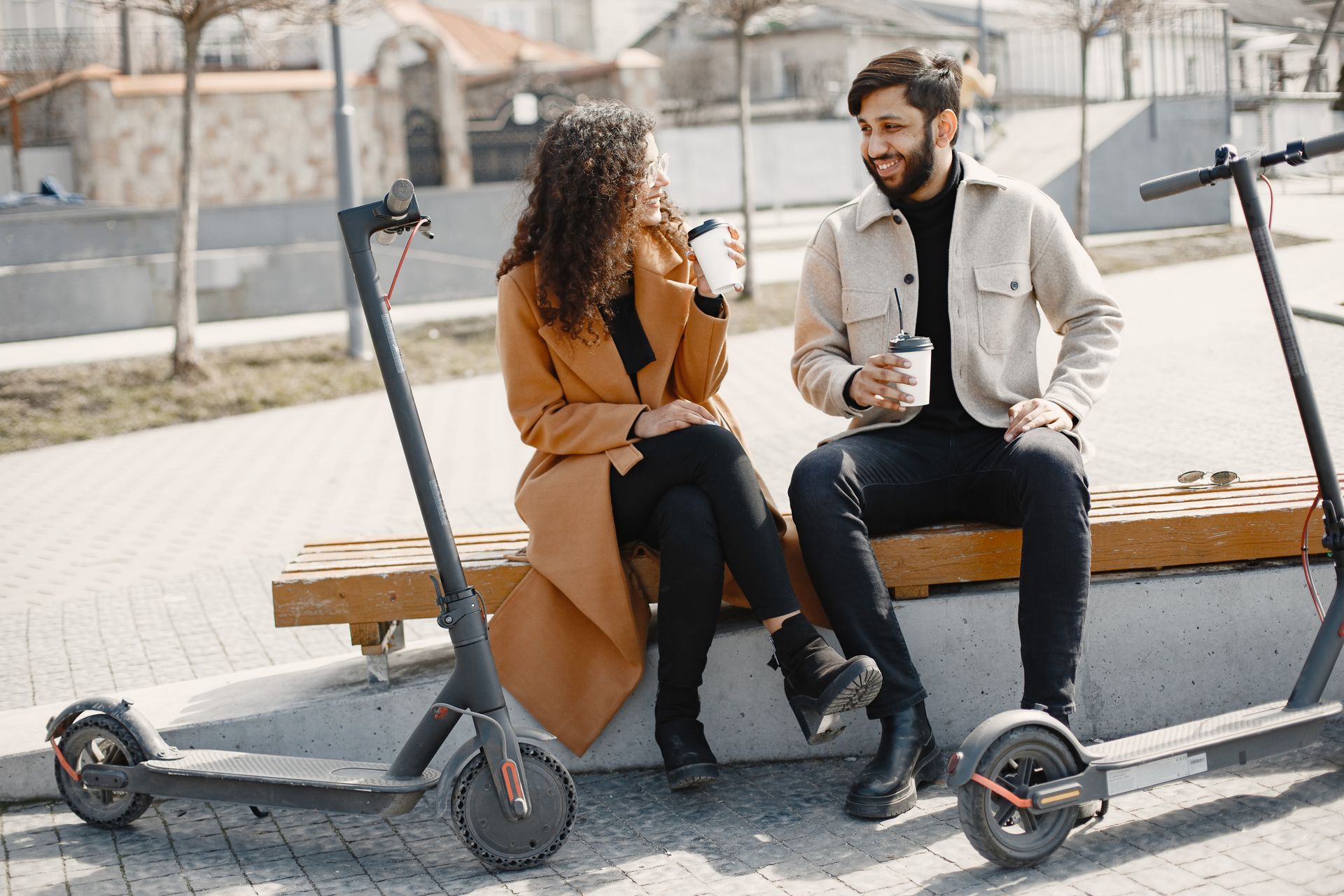 A couple enjoying a break outdoors with electric scooters and drinks, exuding joy and companionship.