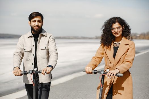 Happy couple riding e-scooters along scenic path on a bright day, embracing leisure and togetherness.
