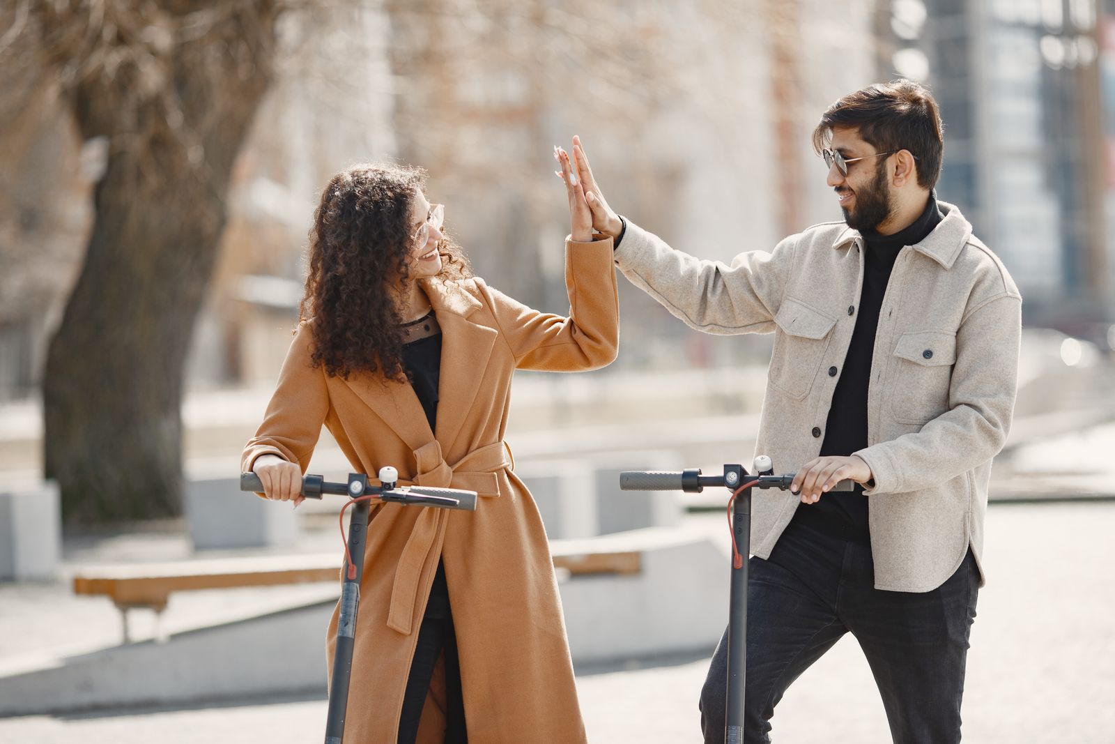 Happy couple sharing a high-five while enjoying a ride on electric scooters in an urban setting.