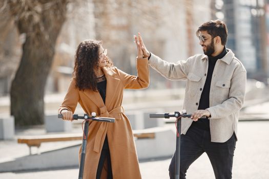 Happy couple sharing a high-five while enjoying a ride on electric scooters in an urban setting.