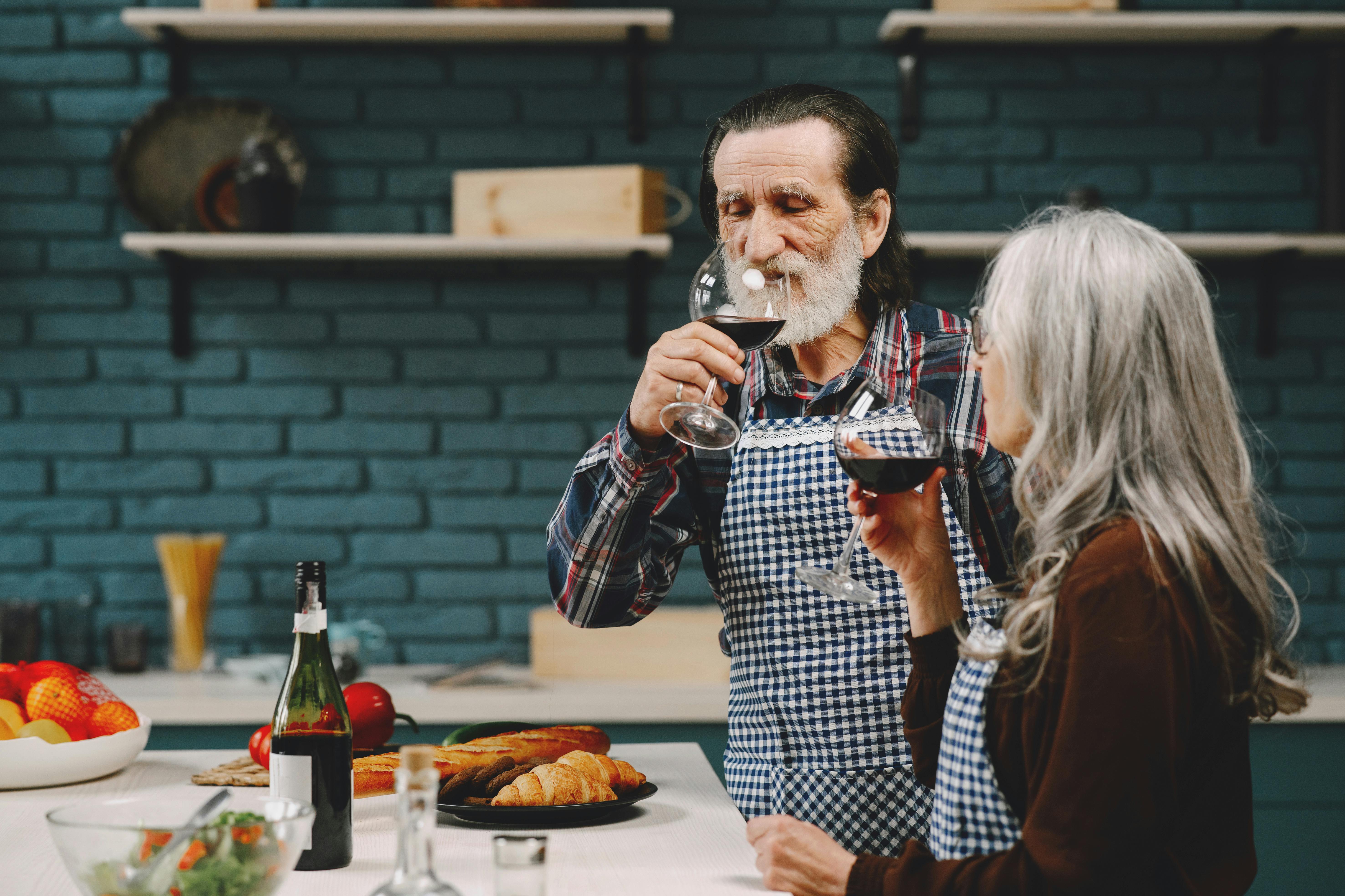 Senior couple savoring red wine in their cozy kitchen with a relaxed atmosphere.