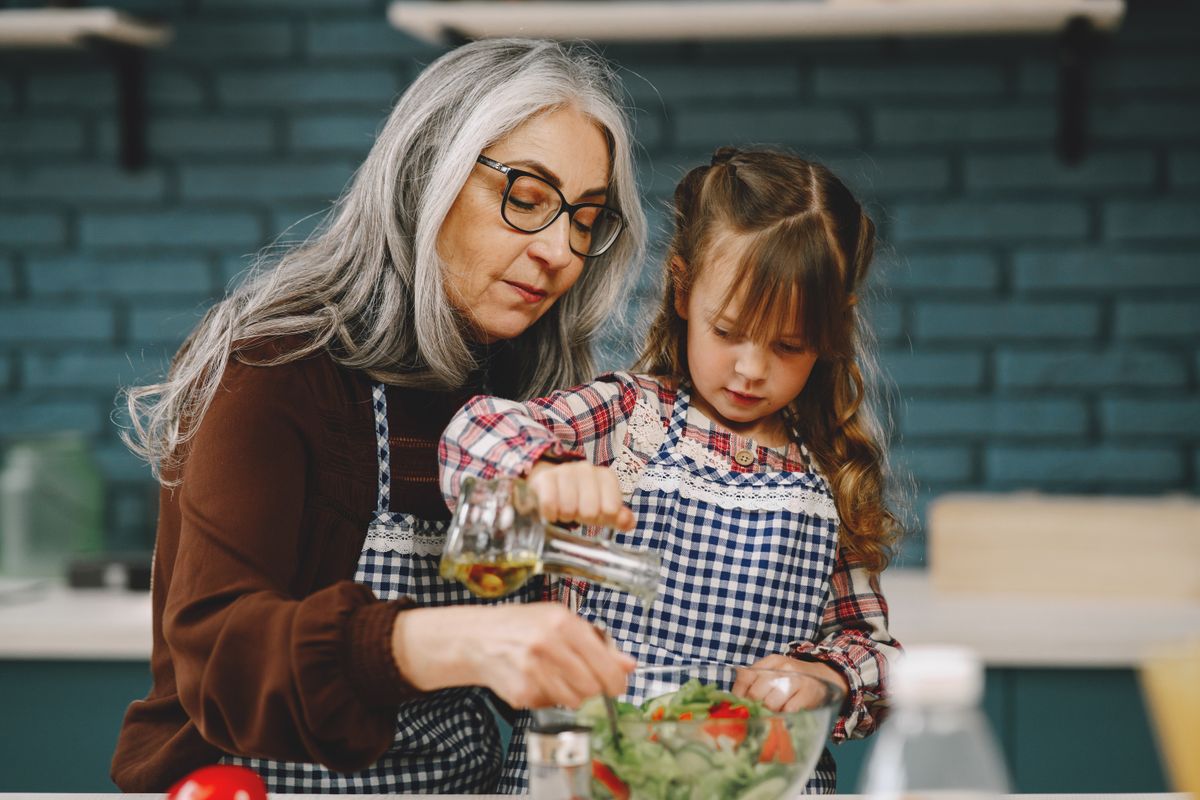 Mujer mayor de cabello gris preparando ensalada fresca en la cocina