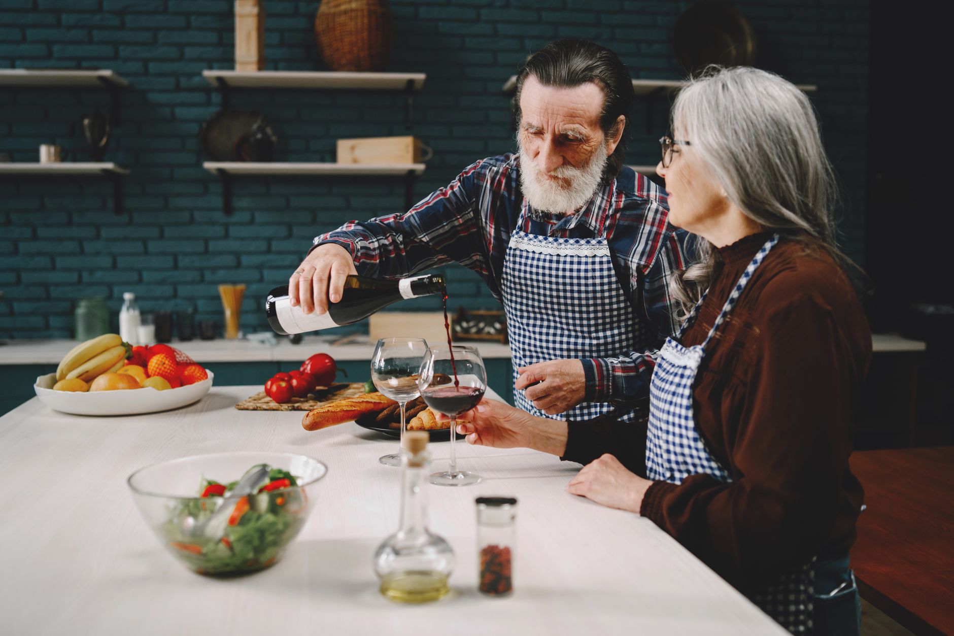 Senior couple savoring wine together in a cozy kitchen setting with fresh produce.