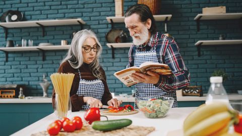 Elderly couple preparing a meal together in a stylish kitchen, emphasizing bonding and teamwork.
