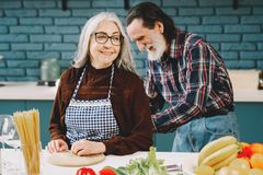 Charming elderly couple bonding while preparing food together in a cozy kitchen.