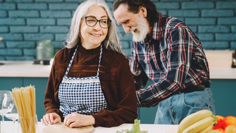 Charming elderly couple bonding while preparing food together in a cozy kitchen.