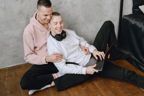 Free Man in White Sweater With Laptop Leaning on a Man in Pink Hoodie  Stock Photo