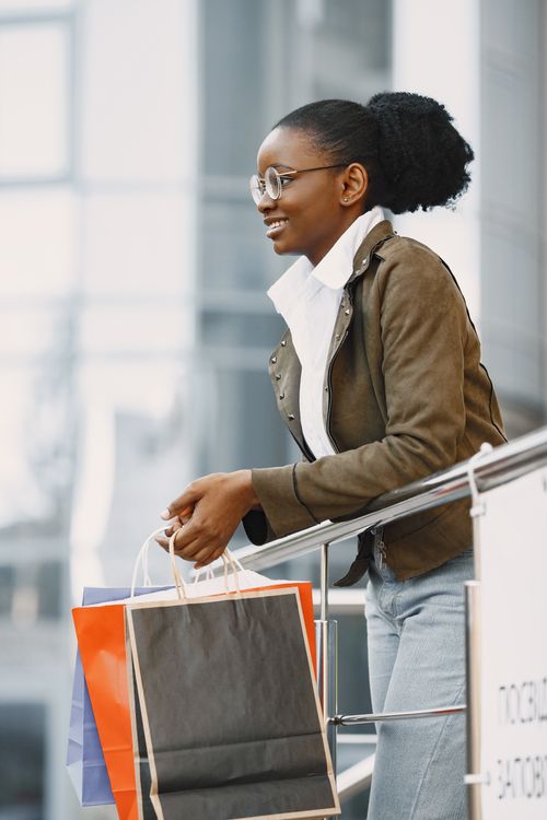 Free Stylish black woman smiling while holding shopping bags in a modern mall setting. Stock Photo