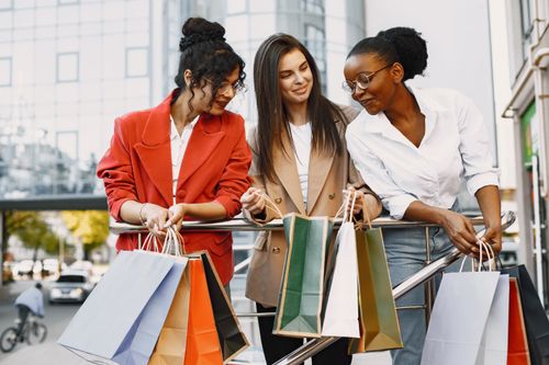 Free Three women enjoying a day of shopping together, holding colorful bags outdoors. Stock Photo