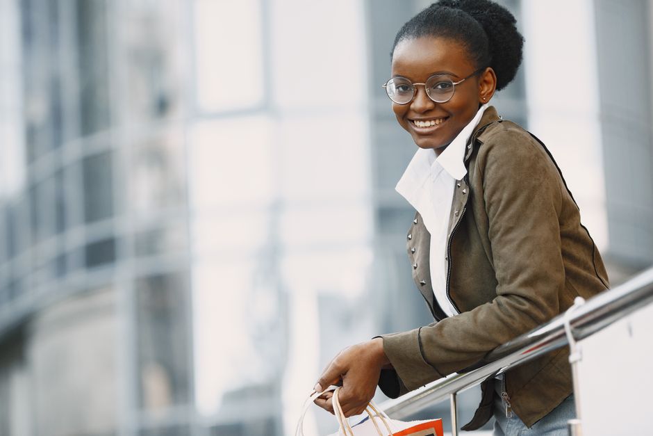 Smiling woman with eyeglasses holding a shopping bag outdoors.