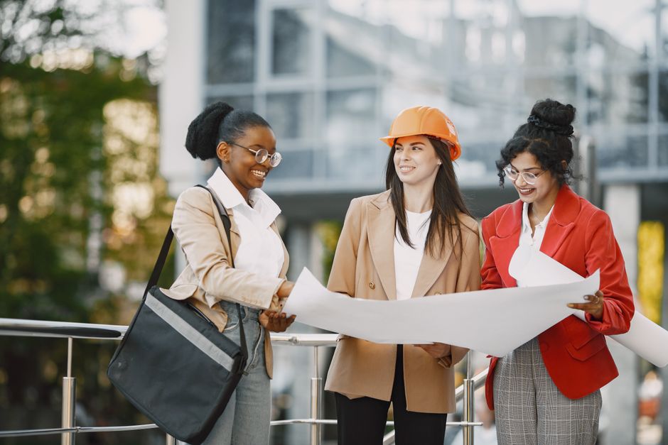 the role of soft skills in digital leadership - Three women collaborating outdoors on architectural plans, showcasing teamwork and diversity.